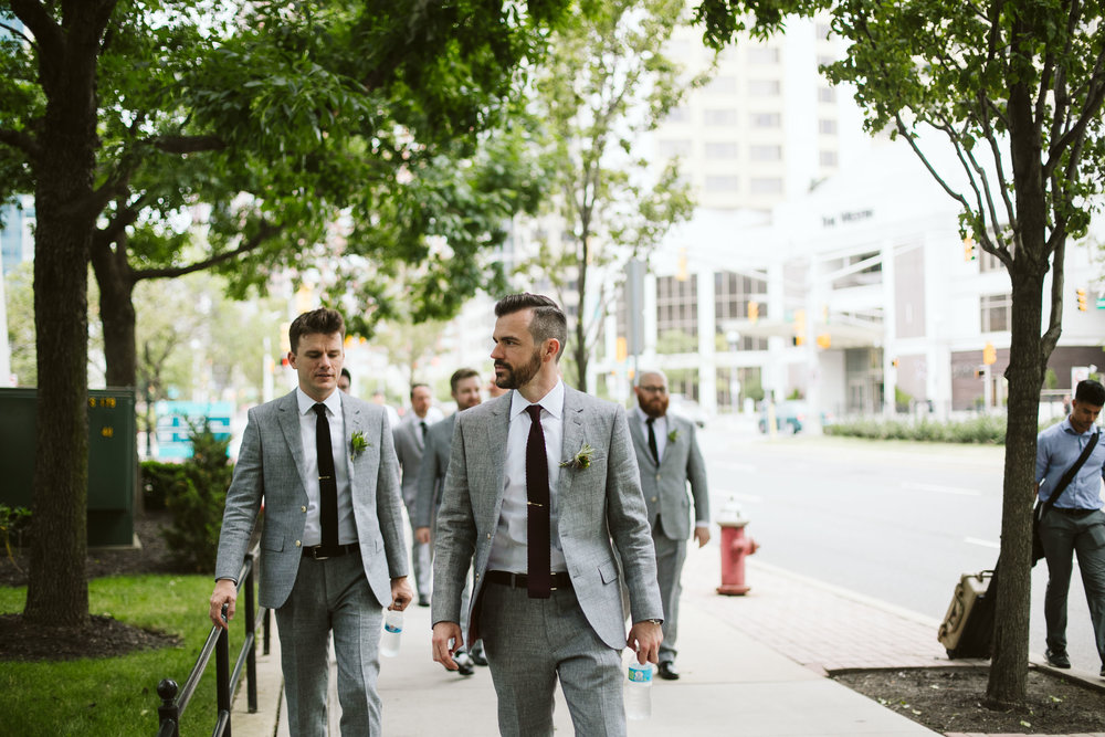  The groom and groomsman walking to the wedding in their gray suits in the city at this Battello Wedding in Jersey City, NJ 