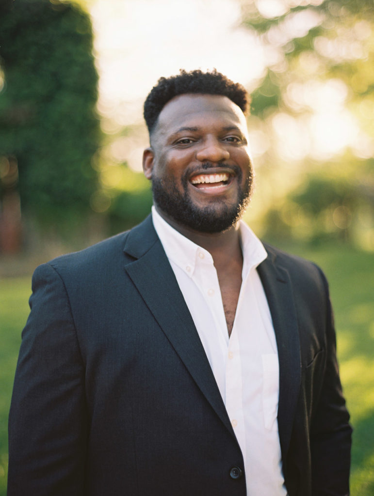 smiling black man wearing a navy suit during engagement session 